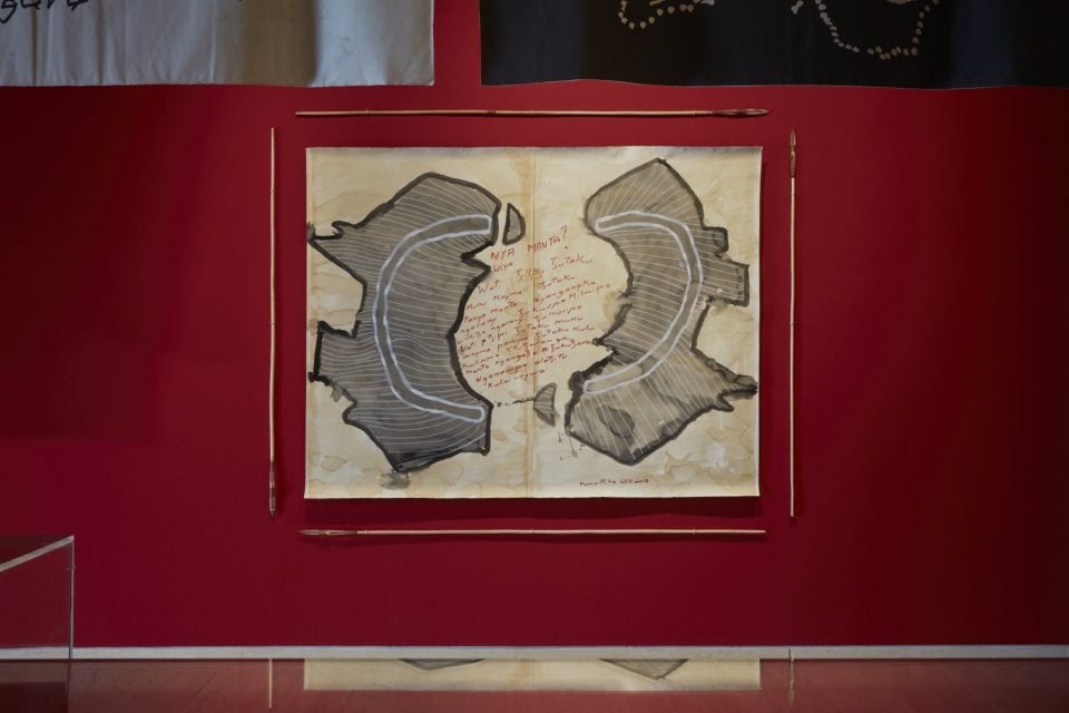 Two paintings depict the outline of the Australian continent. They're rotated and hang on the wall side by side against a dark red wall.