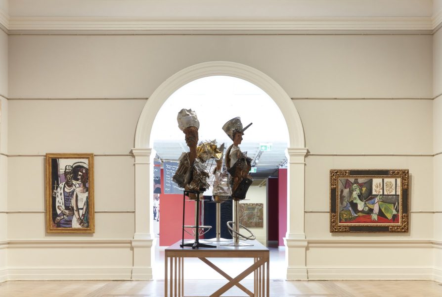 The photo depicts three sculptures by Haitian artist Andre Eugene on a plinth in the middle of the Australian & European modern art collection galleries at the Art Gallery of NSW. The sculptures are contemporary and made of recycled and found objects.