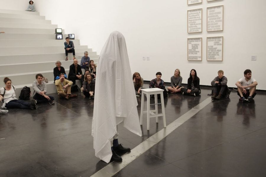 Photograph of Brian Fuata's performance at the Australian Centre for Contemporary Art. The crowd are seated on the floor around the artist.