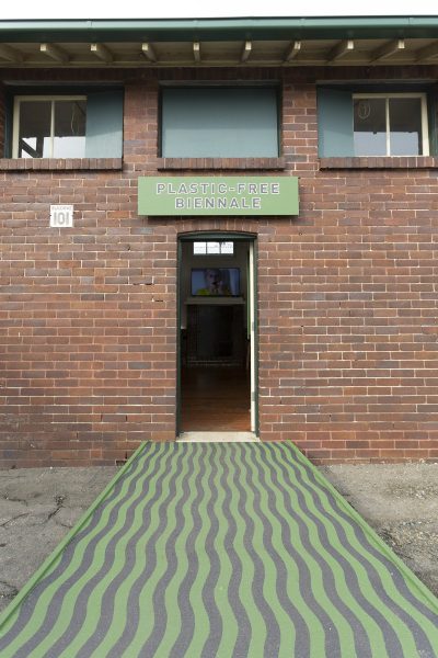 A small brown brick building wth a green and black striped ramp going into the front door. Above the door is a sign reading
