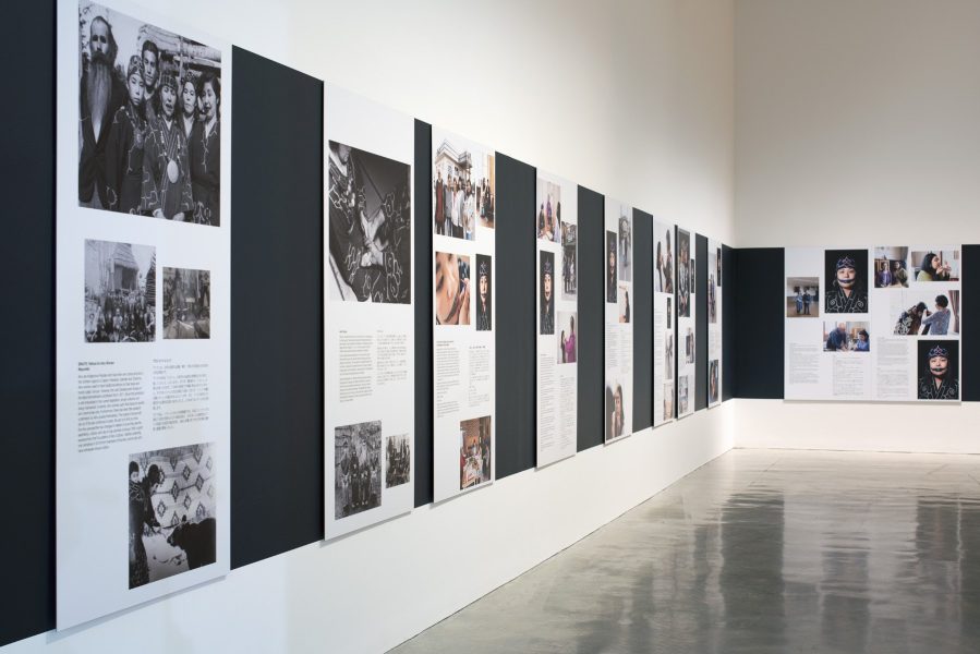 A series of panels with photographs and text are displayed on a wall against a strip of dark charcoal paint. The rest of the gallery wall is white.