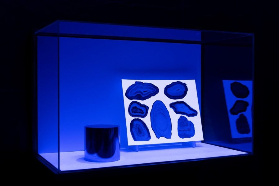 A vitrine with a metal cylinder object in it, alongside an image with the cross section of minerals.